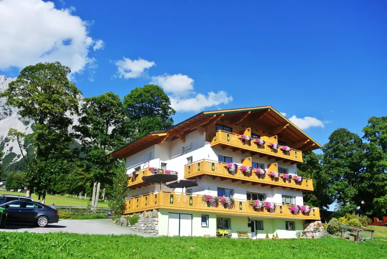 Pension Bergpracht in summer with flower balconies in front of meadows and mountains – summer holiday in Ramsau am Dachstein