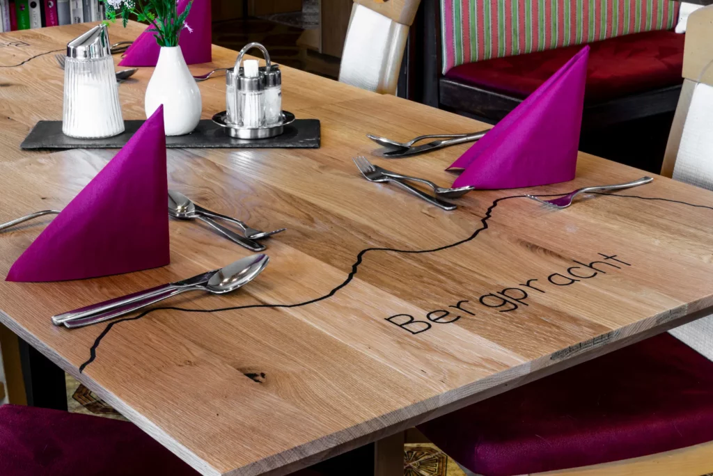 Laid wooden table with Bergpracht engraving in the dining room Laid wooden table with Bergpracht engraving in the dining room – guesthouse in Ramsau am Dachstein